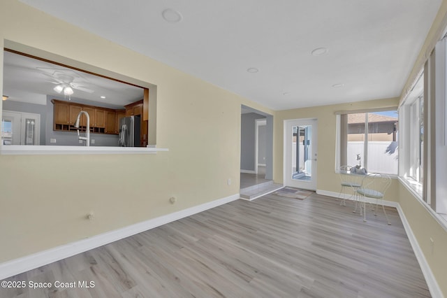 unfurnished living room with baseboards, a ceiling fan, and light wood finished floors