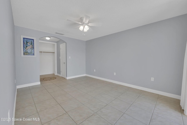 empty room with a ceiling fan, visible vents, baseboards, arched walkways, and a textured ceiling