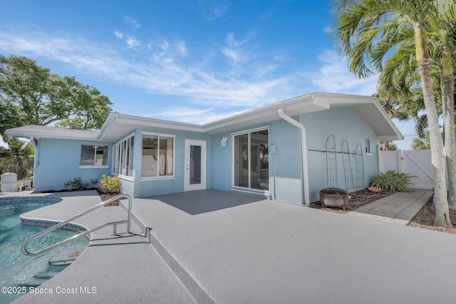 rear view of property featuring fence, stucco siding, a patio area, an outdoor pool, and a gate