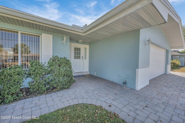 view of exterior entry featuring stucco siding, driveway, and an attached garage