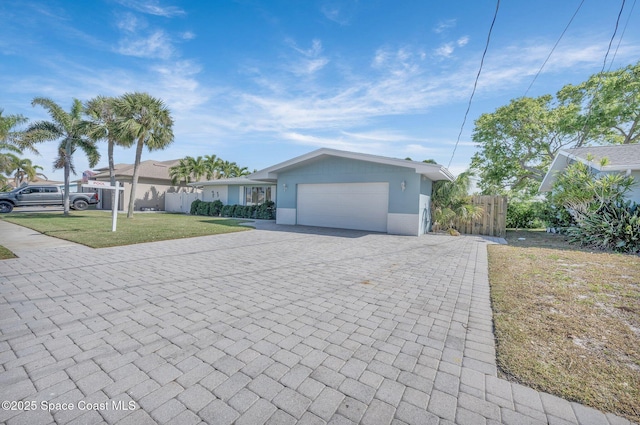 view of front facade with a front lawn, decorative driveway, a garage, and fence