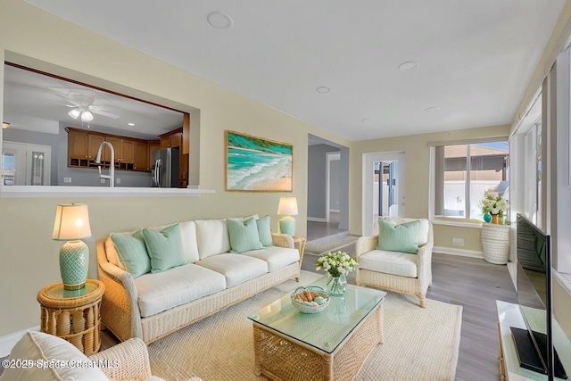 living area featuring baseboards, light wood-type flooring, and ceiling fan
