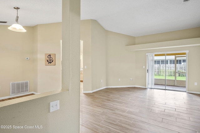 empty room featuring lofted ceiling, baseboards, visible vents, and wood finished floors