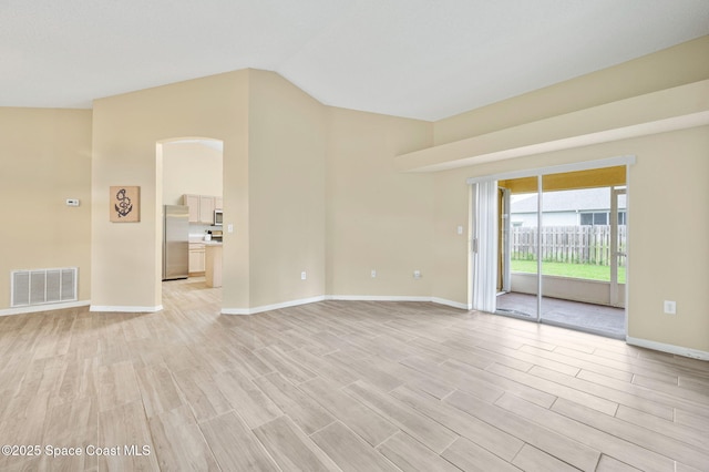 spare room featuring light wood-style floors, baseboards, visible vents, and vaulted ceiling