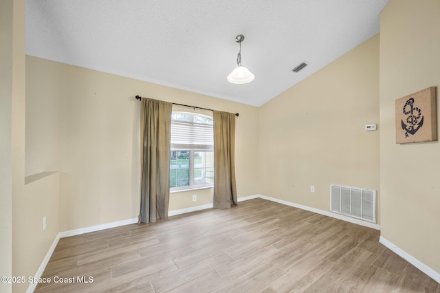 empty room featuring light wood-type flooring, visible vents, vaulted ceiling, and baseboards