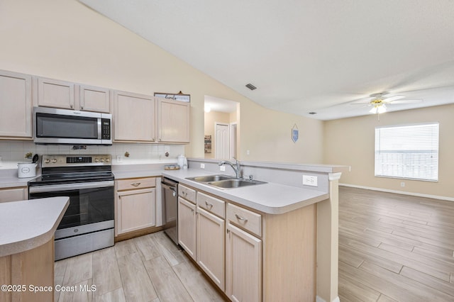 kitchen featuring light countertops, light brown cabinetry, appliances with stainless steel finishes, a sink, and a peninsula