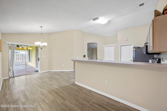 kitchen with lofted ceiling, a peninsula, visible vents, light wood-style floors, and pendant lighting