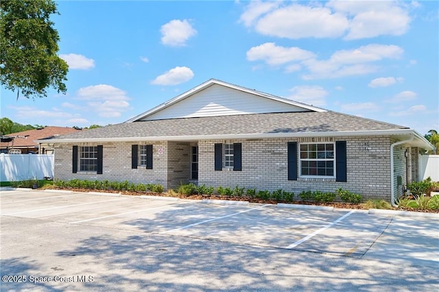 single story home with brick siding, uncovered parking, roof with shingles, and fence