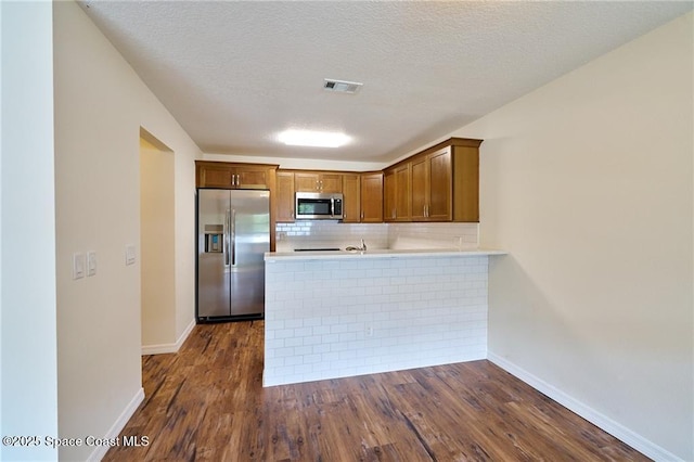 kitchen with dark wood-style floors, visible vents, a peninsula, appliances with stainless steel finishes, and tasteful backsplash