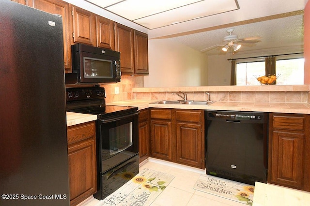 kitchen with light tile patterned floors, a sink, light countertops, backsplash, and black appliances