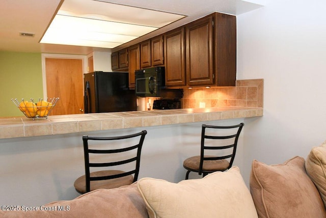 kitchen featuring tile countertops, a breakfast bar area, open floor plan, backsplash, and black appliances