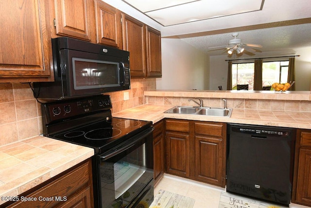 kitchen featuring tile countertops, black appliances, tasteful backsplash, and a sink