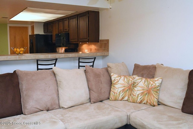 kitchen featuring dark brown cabinetry, a breakfast bar, light countertops, black appliances, and backsplash