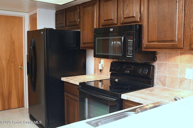 kitchen featuring tile counters, backsplash, black appliances, and light tile patterned floors