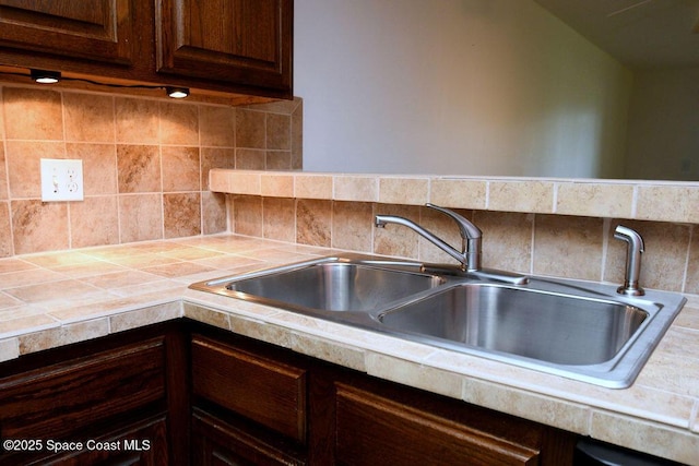 kitchen featuring dark brown cabinetry, tile counters, decorative backsplash, and a sink