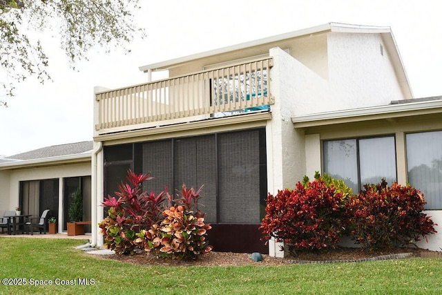 back of house featuring a lawn, a balcony, and stucco siding