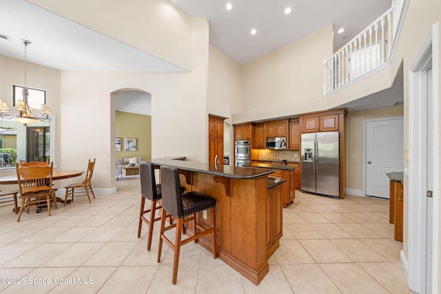 kitchen featuring light tile patterned flooring, arched walkways, a notable chandelier, appliances with stainless steel finishes, and brown cabinetry