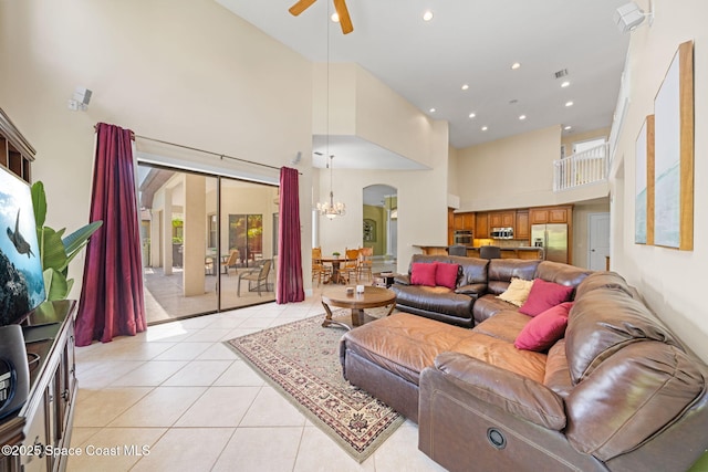 living room with recessed lighting, arched walkways, ceiling fan with notable chandelier, a high ceiling, and light tile patterned floors