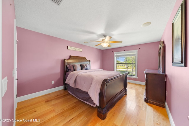 bedroom with a textured ceiling, baseboards, light wood finished floors, and visible vents