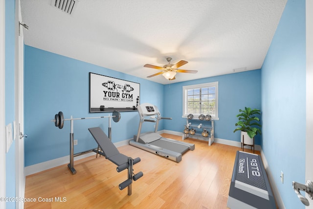 workout area featuring wood finished floors, a textured ceiling, baseboards, visible vents, and ceiling fan