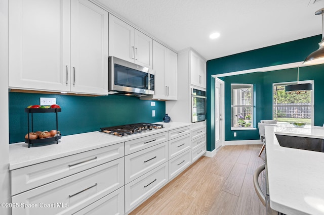 kitchen featuring light wood-style flooring, white cabinetry, baseboards, light countertops, and appliances with stainless steel finishes