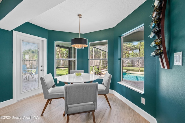 dining area featuring baseboards, a textured ceiling, and light wood finished floors