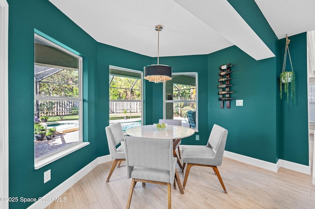 dining room with a textured ceiling, light wood-style flooring, and baseboards