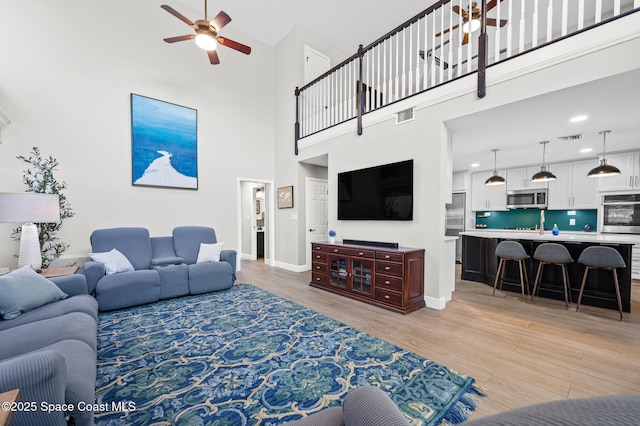 living room featuring light wood-style floors, baseboards, visible vents, and a ceiling fan