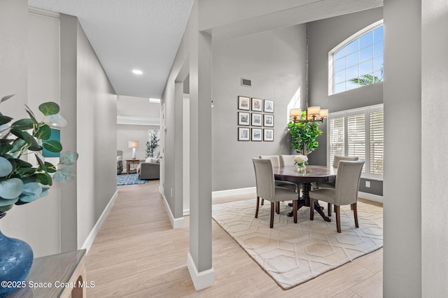 dining area with a towering ceiling, light wood-style flooring, visible vents, and baseboards