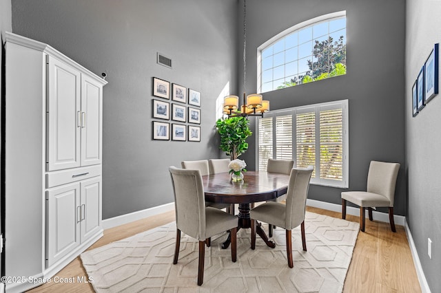 dining space with visible vents, a high ceiling, light wood-style floors, a chandelier, and baseboards