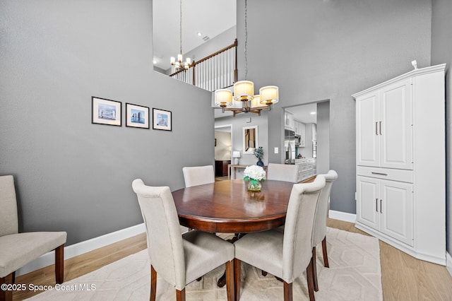 dining space with an inviting chandelier, a high ceiling, baseboards, and light wood finished floors