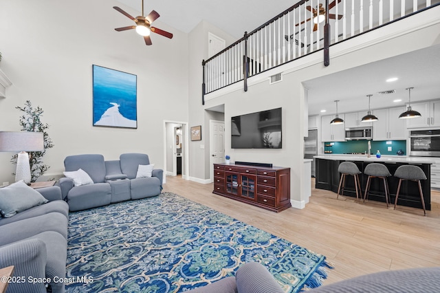 living area with light wood-style floors, visible vents, baseboards, and a ceiling fan