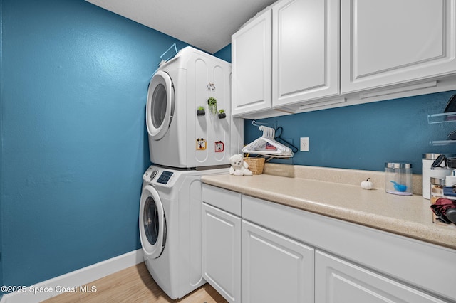 laundry room with light wood finished floors, stacked washer / dryer, cabinet space, and baseboards