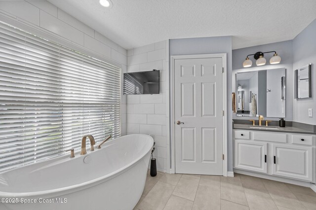 full bathroom featuring tile patterned flooring, a freestanding tub, a textured ceiling, and vanity