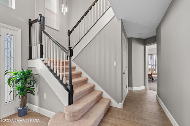 staircase featuring a towering ceiling, baseboards, and wood finished floors