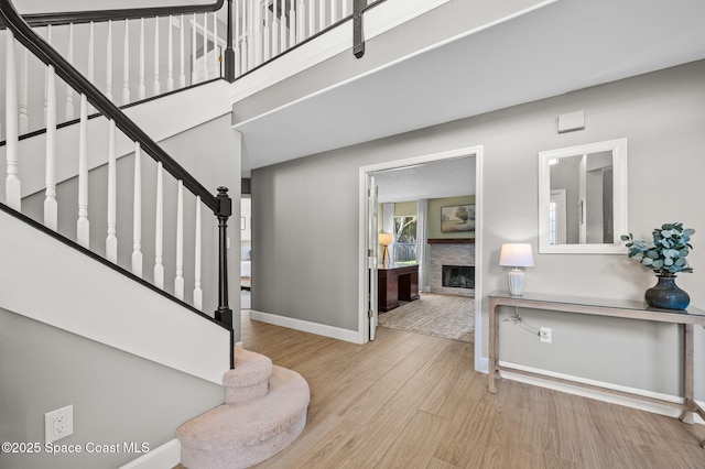 foyer entrance featuring stairs, a fireplace, baseboards, and wood finished floors