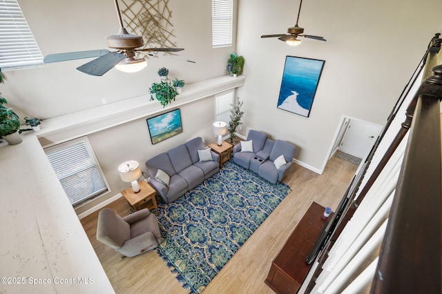 living area featuring ceiling fan, a high ceiling, wood finished floors, and baseboards