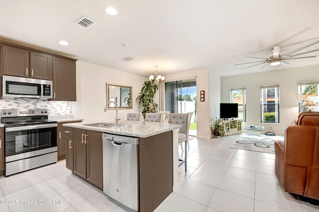 kitchen featuring a center island with sink, open floor plan, a sink, stainless steel appliances, and backsplash