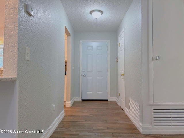 entryway with a textured ceiling, a textured wall, wood finished floors, and visible vents