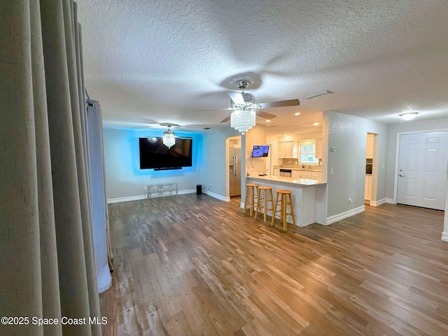 unfurnished living room with baseboards, a textured ceiling, a ceiling fan, and wood finished floors