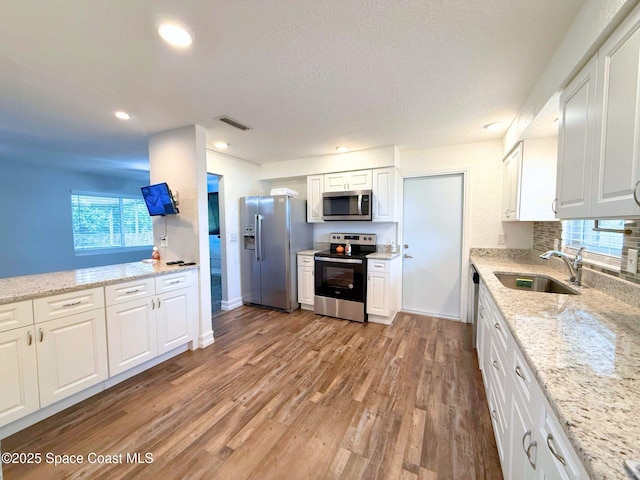 kitchen featuring visible vents, white cabinets, appliances with stainless steel finishes, light wood-style floors, and a sink