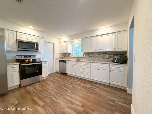 kitchen with stainless steel appliances, white cabinetry, decorative backsplash, and wood finished floors