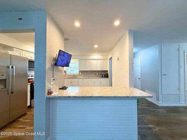 kitchen with white cabinets, a textured wall, dark wood-style floors, light stone counters, and stainless steel appliances