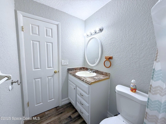 bathroom with a textured wall, vanity, toilet, and wood finished floors