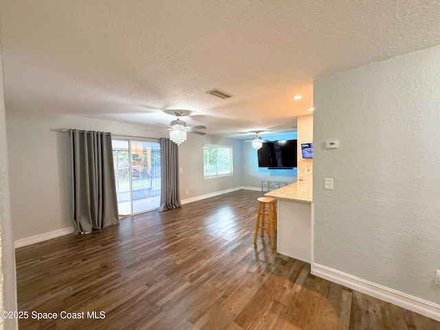 living room featuring dark wood-type flooring, visible vents, a textured ceiling, and baseboards