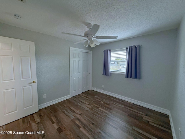 unfurnished bedroom with a closet, a textured ceiling, baseboards, and wood finished floors