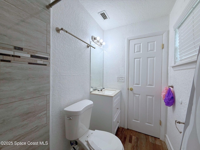 bathroom with toilet, visible vents, wood finished floors, and a textured wall