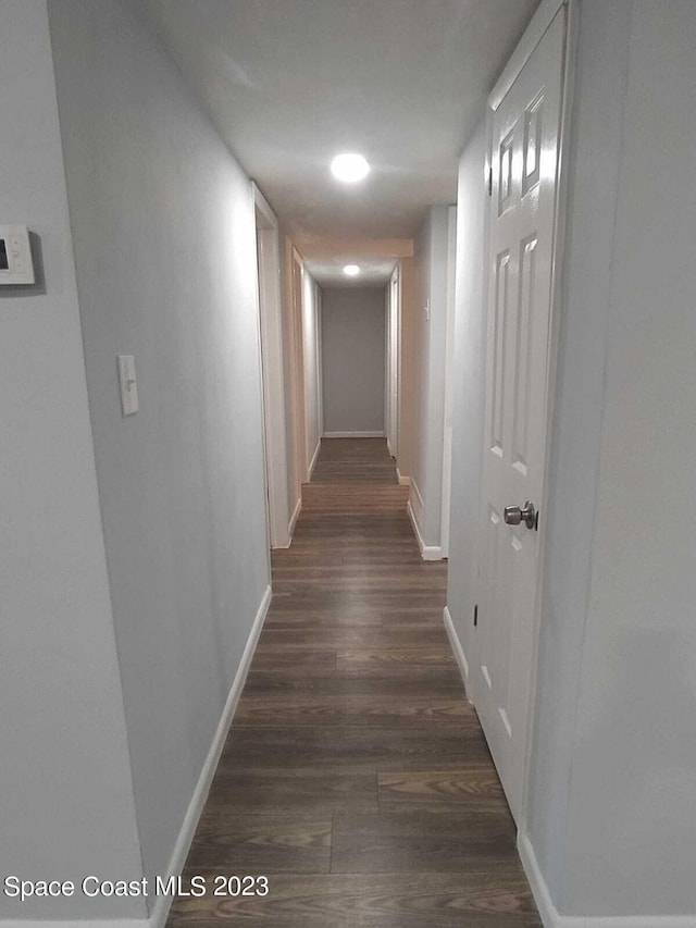 hallway featuring dark wood-type flooring and baseboards