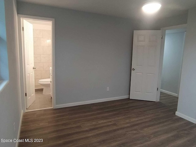 unfurnished bedroom with connected bathroom, dark wood finished floors, tile walls, and baseboards