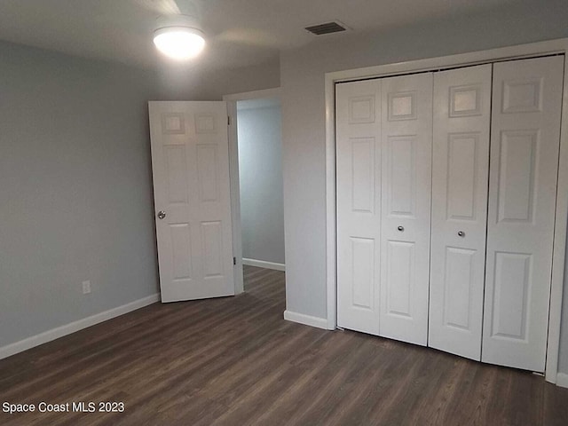 unfurnished bedroom with dark wood-type flooring, a closet, visible vents, and baseboards